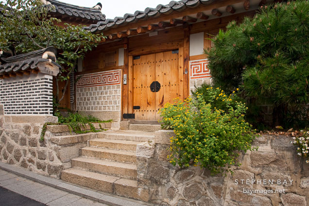 The distinctive traditional Korean hanok (house) features a wooden door, block and beam construction, and a tile roof.