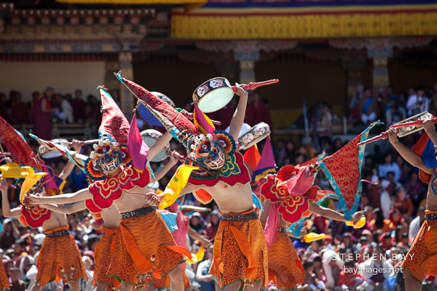 Ging dancers wearing masks, orange skirts, and flags atop their heads. Thimphu tsechu, Bhutan.