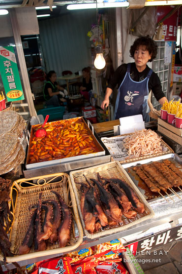 Woman selling tteokbokki (spicy rice cakes), dried squid, and octopus at a food stand.  Incheon, South Korea.