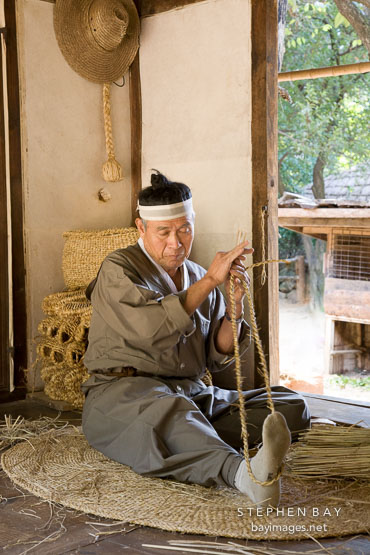 A Korean man weaves sandals from straw. Korean Folk Village, South Korea.