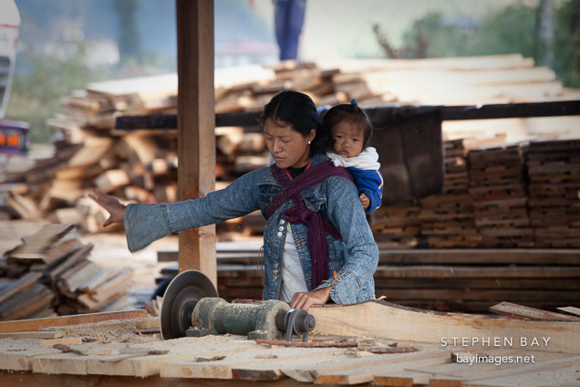 Woman with baby sawing lumber. Paro, Bhutan.