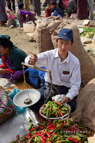 Man weighing chili peppers for sale at the weekend market. Punakha, Bhutan.