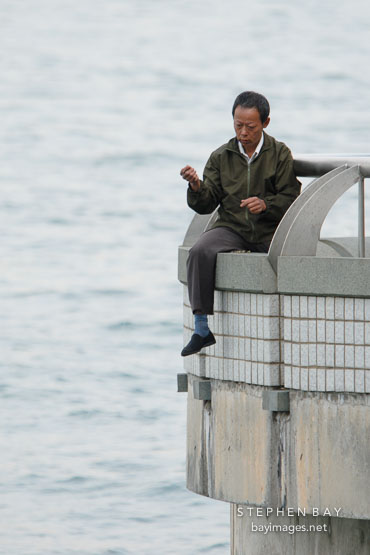 Man fishing with a bare line from railing. Hong Kong, China.
