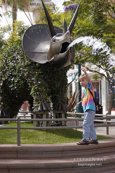 Boy reaching for the water fountain. Triceratops. Third Street Promenade, Santa Monica, California, USA.