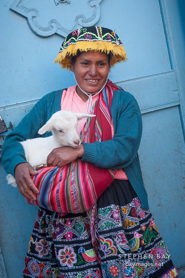 Woman in traditional dress holding baby goat. Pisac market. Sacred Valley, Peru.