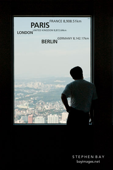 A man is silhouetted against a window in Seoul Tower on Namsan. He is looking out over the city of Seoul, South Korea.