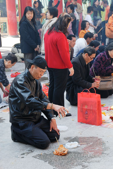 Man pouring alcohol and offering food for the deceased. Wong Tai Sin Temple, Hong Kong, China.