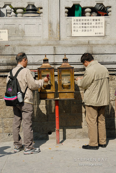Two men lighting incense at the Wong Tai Sin Temple. Hong Kong, China.