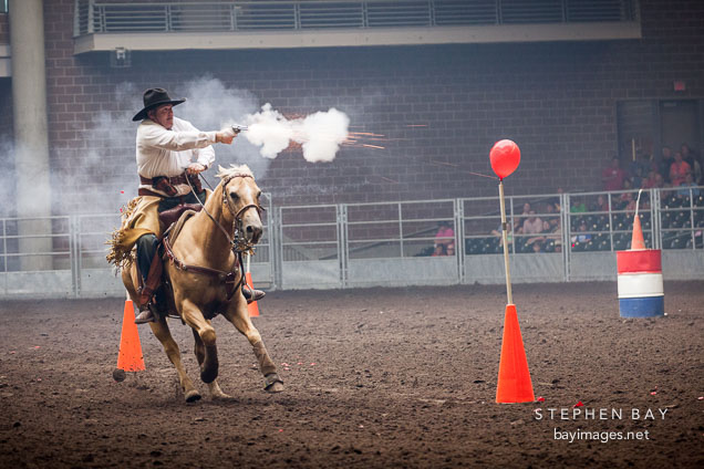 Cowboy fires gun at balloon targets during the mounted shooting contest. Iowa State Fair, Des Moines.