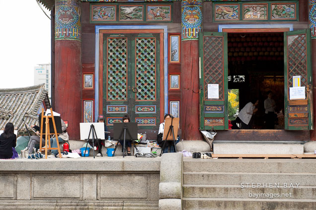 Art students work outside Daewoongjeon, the main temple located at Bongeunsa in Seoul. Daewoong means big hero and is another name for Buddha. The building houses statues of Sakyamuni Buddha, Amitabha Buddha, and Bhaisagya Buddha.