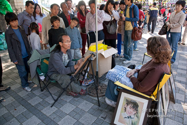 An artist draws a pastel portrait of a tourist outside N Seoul Tower, gathering a crowd.