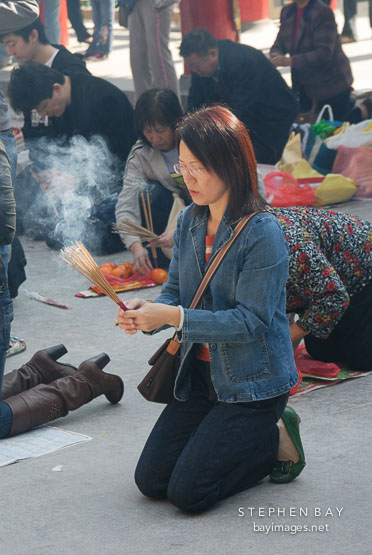 Woman praying with incense sticks. Wong Tai Sin Temple, Hong Kong, China.