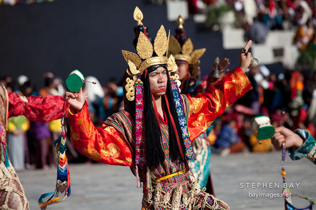 Dancer with gold crown and damaru in the right hand and dribu in the left. Thimphu tsechu, Bhutan.