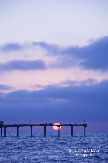 Setting sun just over the horizon at Ocean beach pier. San Diego, California.